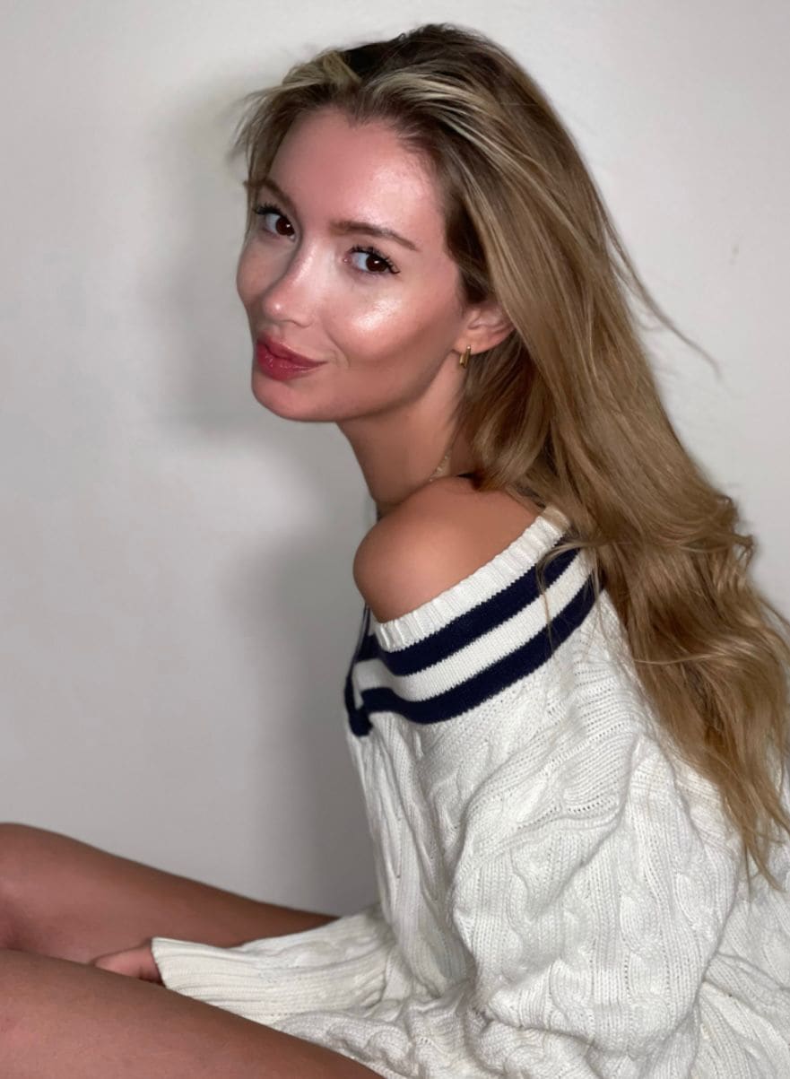 Clara seated in an off-shoulder white cable-knit sweater with navy stripes.