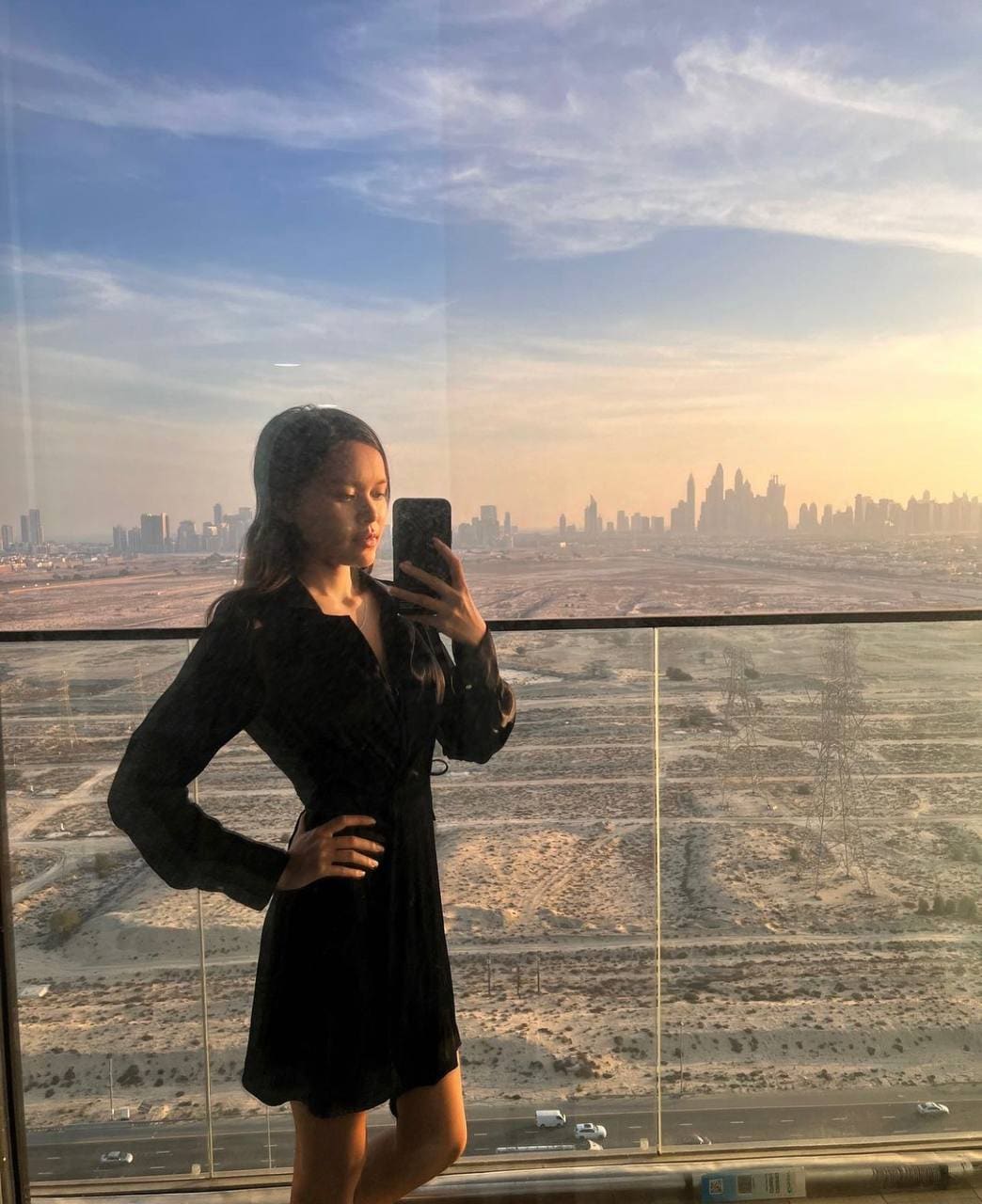 Selfie frente a espejo con vestido negro de manga larga, atardecer urbano.