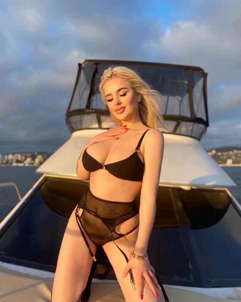 Mujer rubia en traje de baño negro de dos piezas con paneles translúcidos en cubierta de barco.