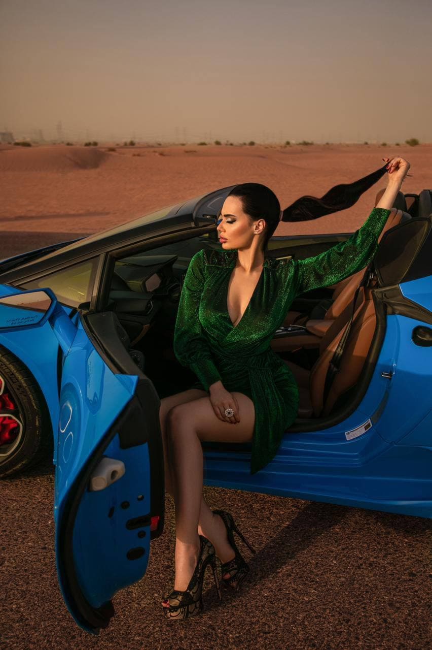 Anna en el marco de una azul deportiva en el desierto, con vestido verde y bufanda negra alzada.