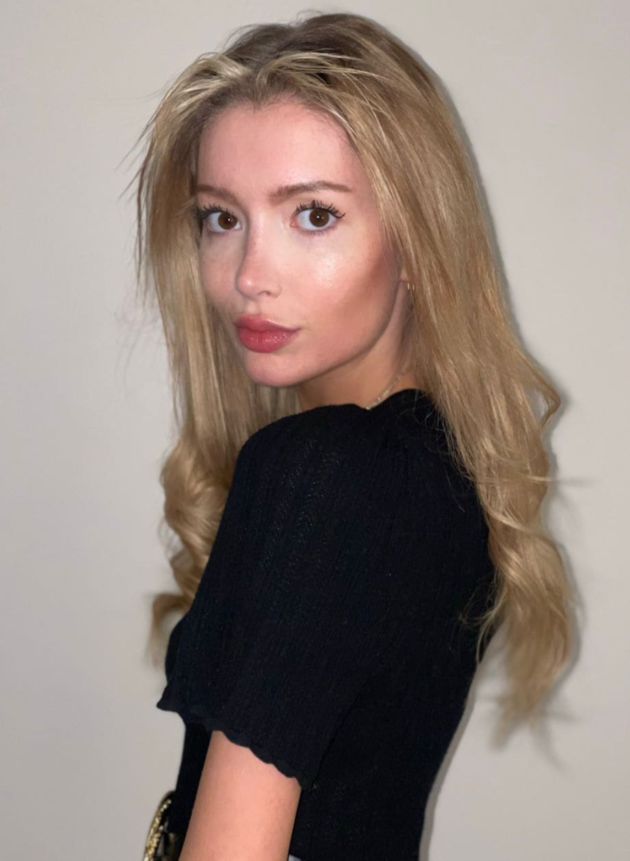 Side view of Clara in a short-sleeved black ribbed top against a plain wall.