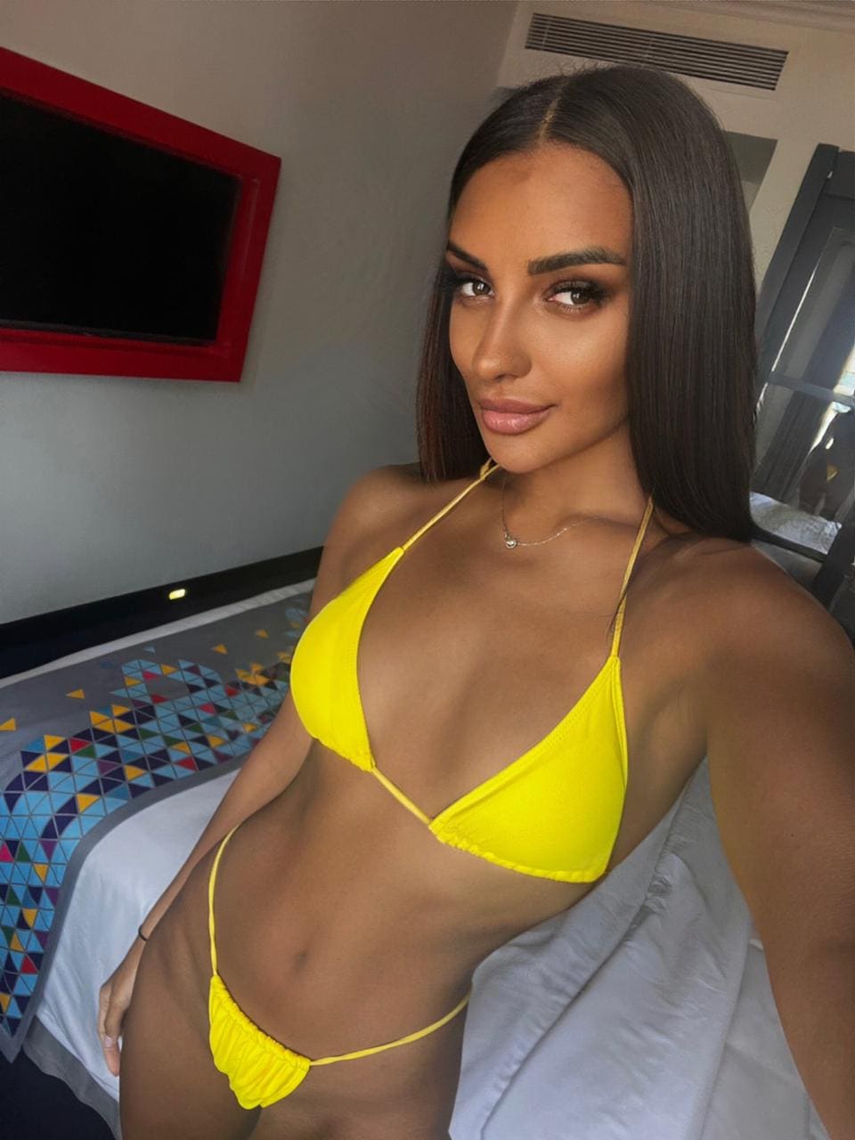 Mujer en dormitorio con bikini amarillo, mano en cadera frente a espejo rojo.