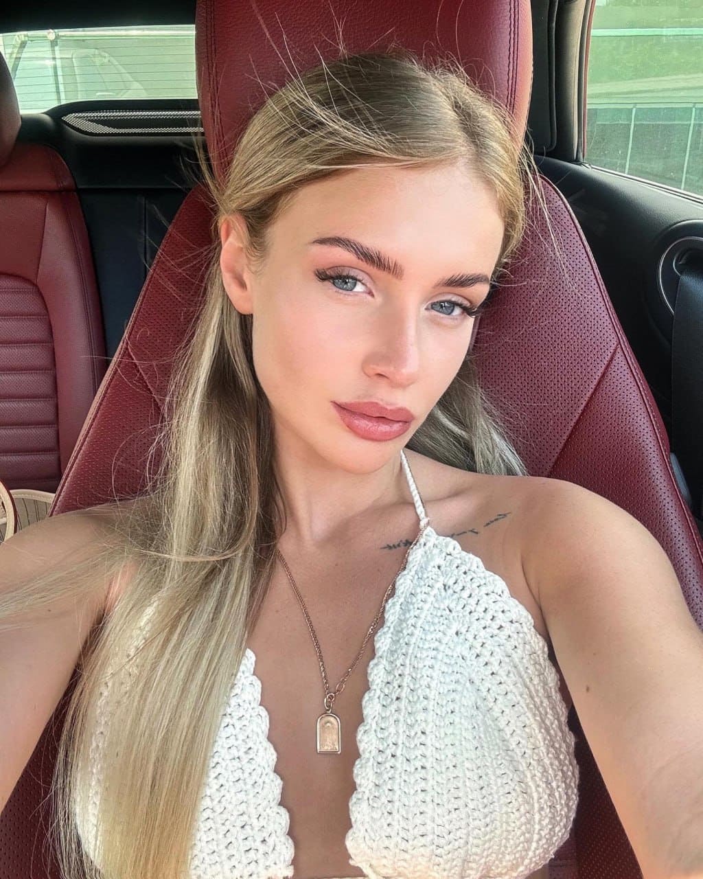 Mujer rubia sentada en el asiento del conductor, con top blanco crochet y asiento rojo.
