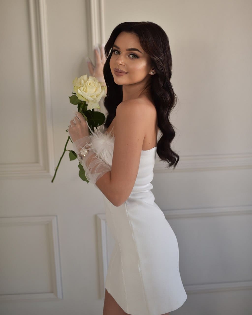 Profilo di donna in miniabito bianco e guanti piumati, che regge un mazzo di rose bianche.