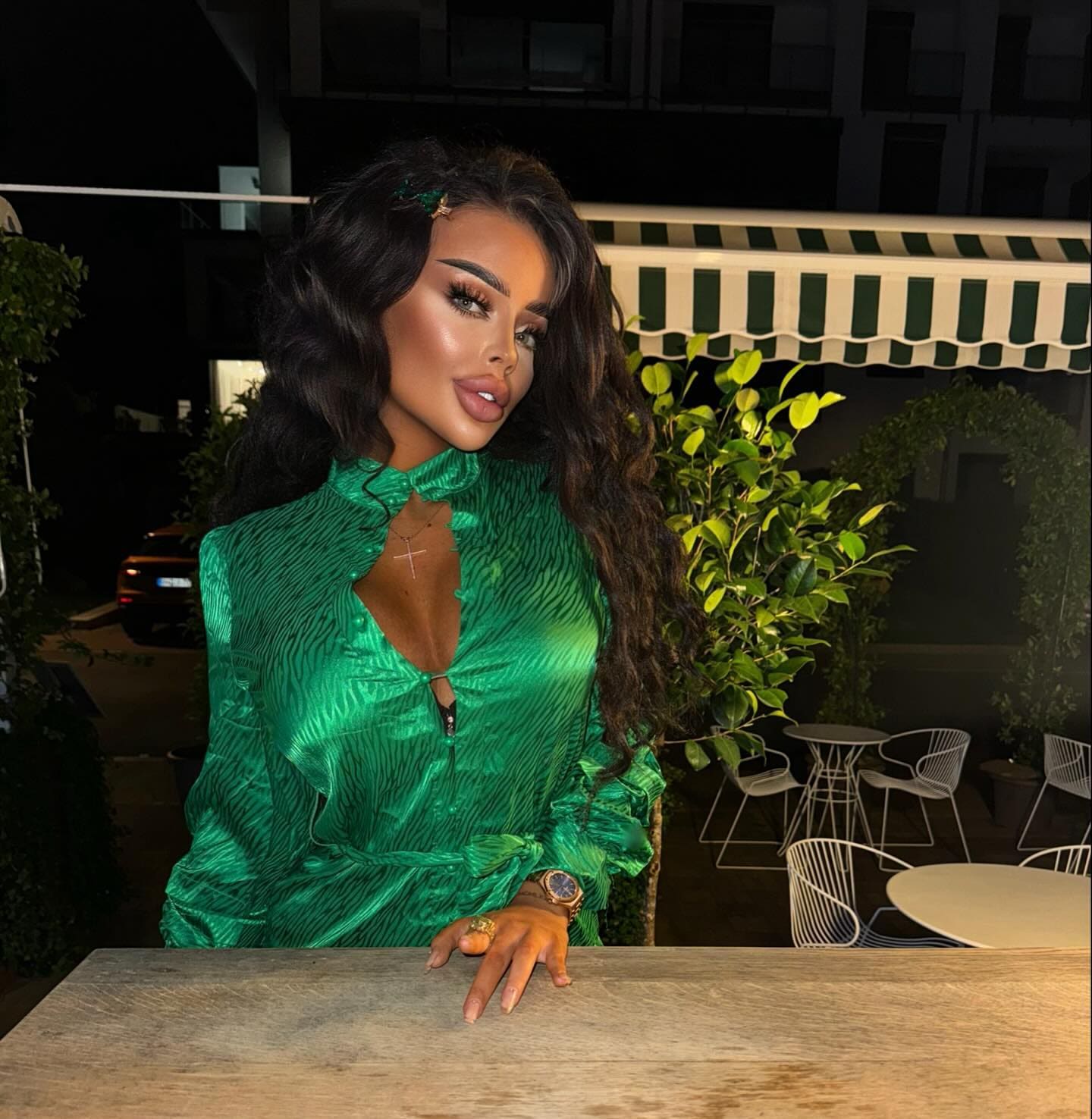 Mujer al aire libre de noche con blusa verde brillante y collar, junto a una mesa de madera.