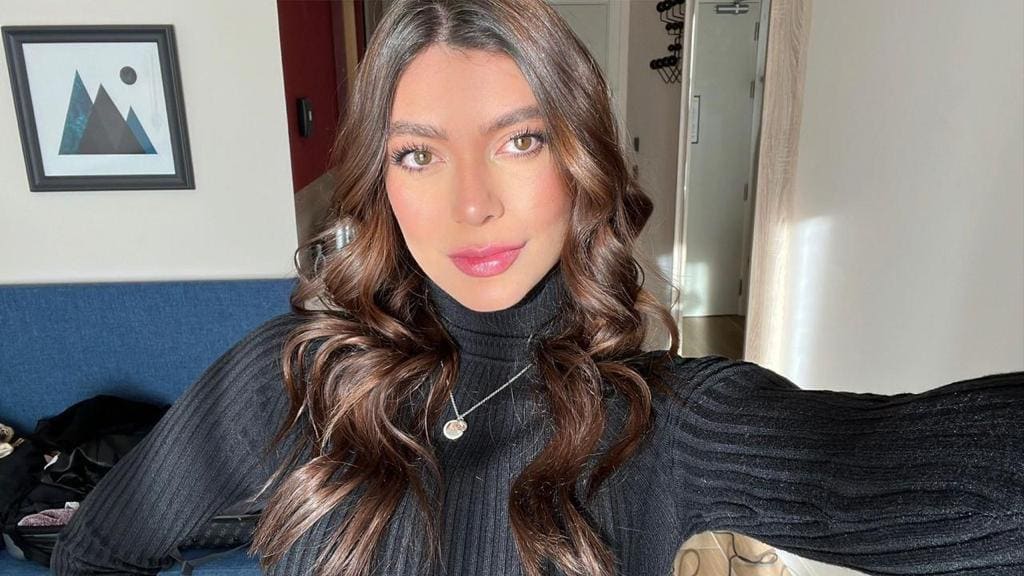 Mujer sentada en interior con jersey negro de cuello alto y sofá azul detrás.