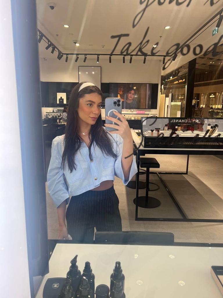 Selfie en espejo de tienda con chaqueta vaquera azul claro, banda blanca y pantalón.