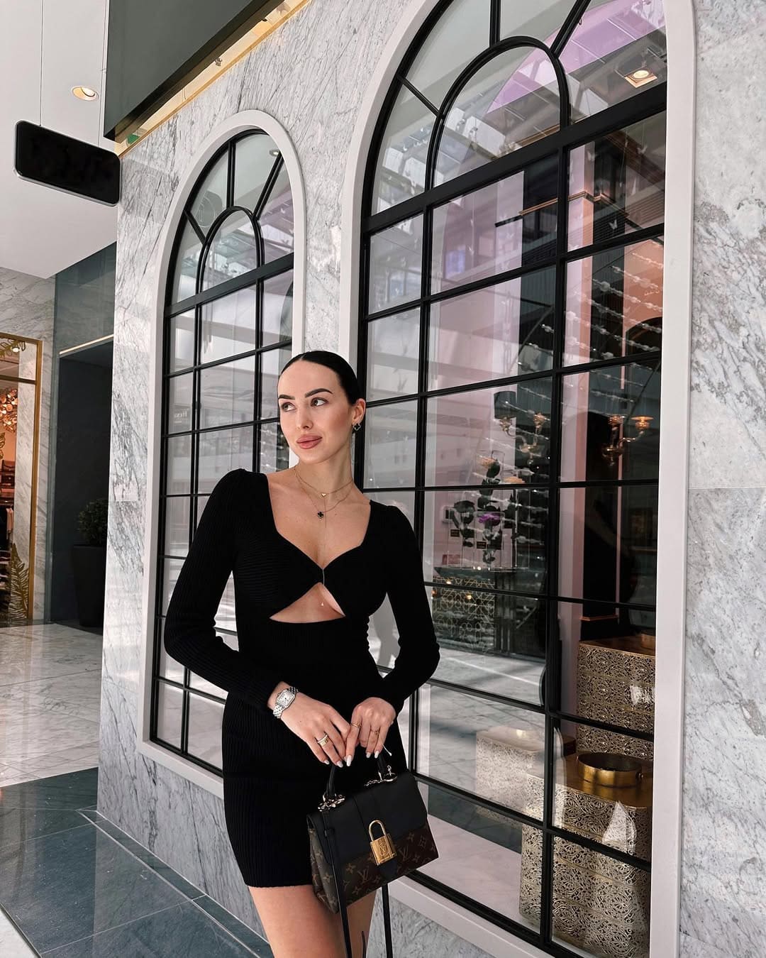 Mujer de mini vestido negro con bolsillo estampado en interior de mármol y arcos.