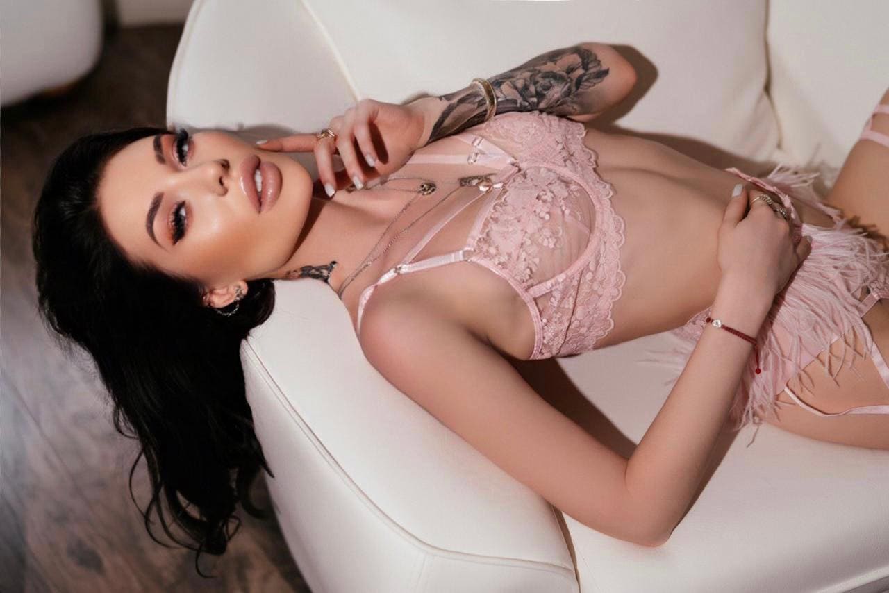 Mujer tumbada en sofá blanco con conjunto rosa encajado, una mano cerca de la cara y otra en la cadera.
