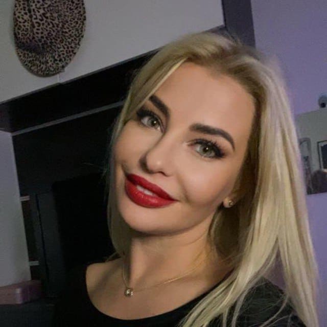 Retrato cercano de mujer rubia con labial rojo, collar fino y fondo decorado con leopardo.
